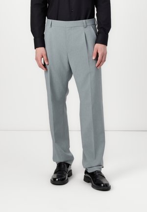 Light gray pleated trousers made of smooth fabric, featuring a tailored fit and side pockets, paired with black dress shoes.