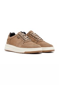Zapatillas de ante marrón con una suela de goma blanca contrastante, punta redondeada y diseño con cordones. Presenta detalles en la parte superior y acentos negros.