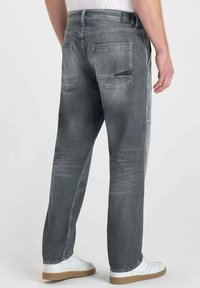 Jean en denim gris à coupe décontractée, comportant deux poches arrière et une légère texture décolorée. Associé à des baskets blanches et un haut simple.