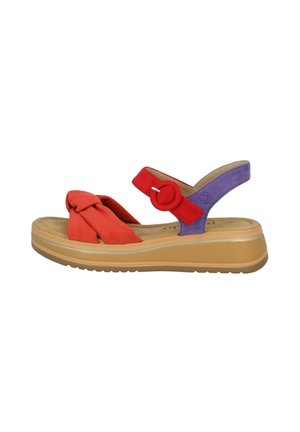 Red and purple suede women’s sandal with a knotted front strap, a circular accent, and a thick beige rubber sole. Features an adjustable heel strap.