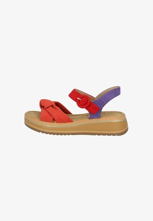 Red and purple suede women’s sandal with a knotted front strap, a circular accent, and a thick beige rubber sole. Features an adjustable heel strap.