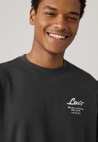 Sudadera de cuello redondo de algodón negro con el logo y texto en blanco de Levi's en el lado izquierdo del pecho, que destaca por su textura suave y ajuste holgado.