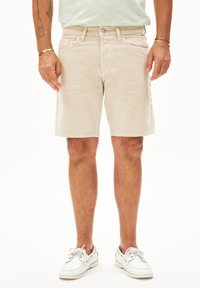 Beige denim shorts met een klassieke pasvorm, vijf zakken en een knoopsluiting; gedragen met witte bootschoenen. Gladde textuur, casual ontwerp.