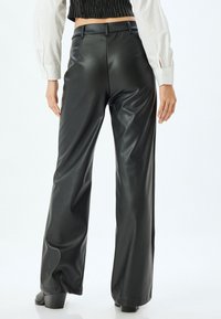 Zwarte faux leren wijde broek met een hoge taille, een zachte textuur en subtiele glans. De broek heeft riemlussen en een getailleerde pasvorm aan de achterkant.