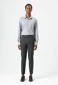 Lichtgrijs shirt met lange mouwen en een button-down kraag, gecombineerd met op maat gemaakte donkergrijze broek en zwarte schoenen. Soepele texturen en een strakke pasvorm.