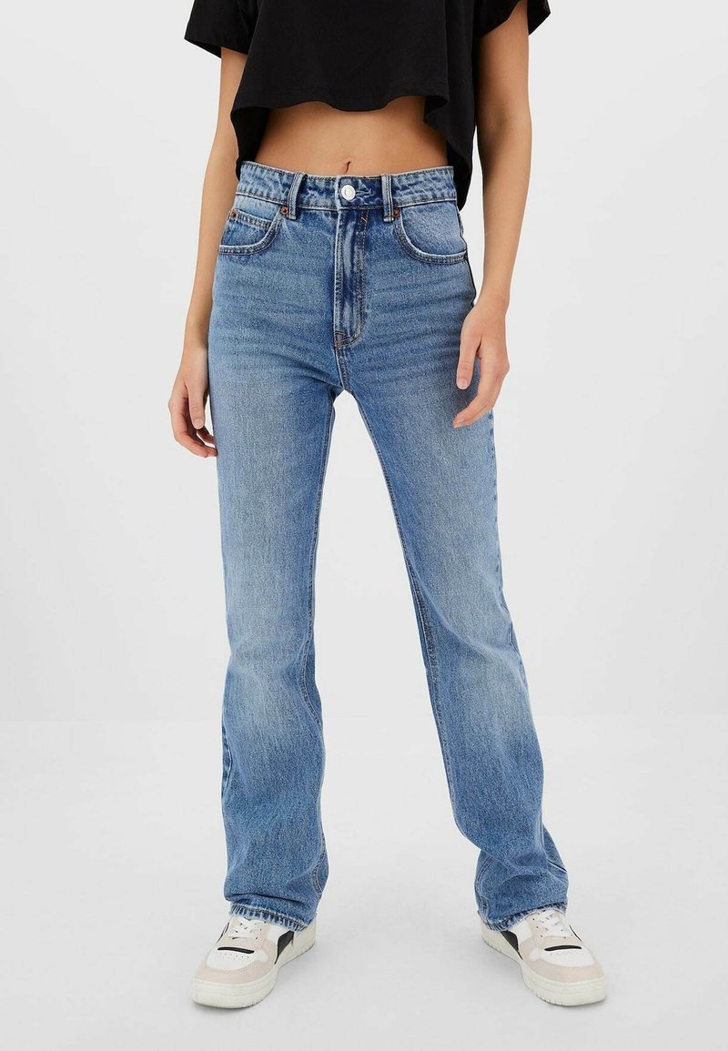 Jeans azzurri chiaro a vita alta con gamba dritta, caratterizzati da tasche frontali, leggero scolorimento e orlo grezzo, abbinati a sneakers bianche.