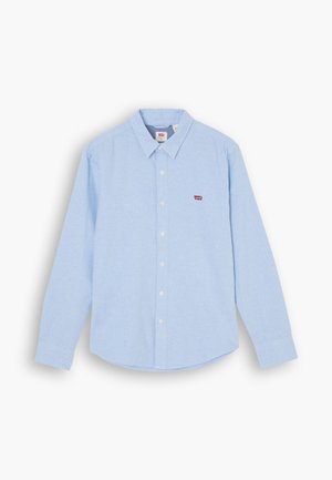 Světle modrá košile s dlouhým rukávem, měkká textura, špičatý límec a malé červené logo na levé části hrudi.