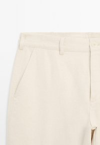 Beige cotton trousers with a flat front, belt loops, two angled front pockets, and a button closure. Smooth texture and tailored design.