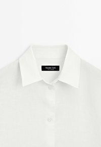 Weißes Leinenhemd mit klassischem Kragen, Knopfleiste und einem Etikett mit dem Text "Massimo Dutti". Glatte Textur, minimalistisches Design.