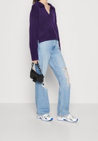 Lila stickad tröja med V-ringning och krage, ljusblå slitna raka jeans, vita och blå sneakers samt en liten svart handväska.