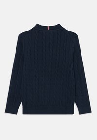 Granatowy sweter z dzianiny w warkocze z długimi rękawami i ściągaczami, z małym detalem w postaci czerwono-biało-niebieskiego paska na plecach przy kołnierzu.