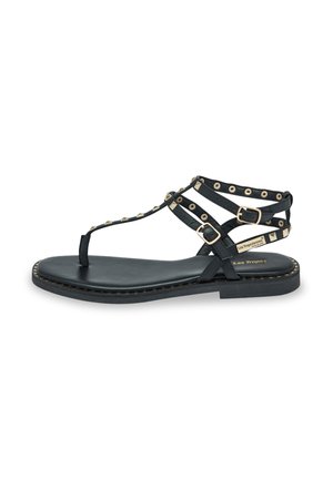 Black sandal with flat sole and T-strap design. Features gold decorative studs and buckle accents. Made of smooth leather with a stitched edge.