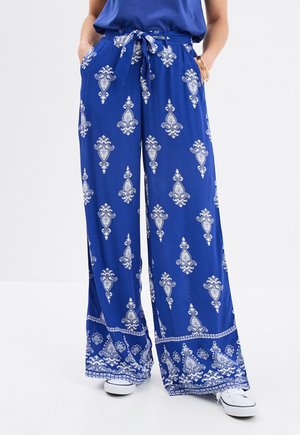Blaue weite Hosen mit einem gebundenen Taillenbund, die weiße Dekormuster und einen Besatz entlang des Saums aufweisen, aus einem leichten Stoff gefertigt.