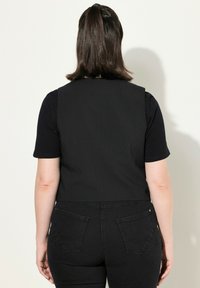 Svart ärmlös väst med skräddarsydd design, bärs över en svart t-shirt, paras med svarta jeans som har bakfickor och en slät yta.