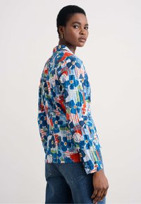 Chemise à boutons avec un motif floral coloré aux nuances variées de bleu, rouge et vert ; détails de col et d fente latérale ; tissu léger.