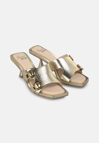 Mule aperti in metallo dorato con punta quadrata, due ampie cinghie con fibbie dorate e un tacco sottile. Fodera con una soletta in beige chiaro.