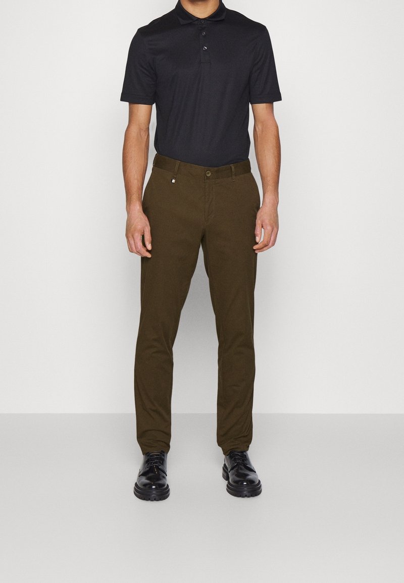 Polo noir à manches courtes associé à un pantalon vert olive. Le pantalon présente une coupe standard et une fermeture par bouton. Des chaussures noires complètent la tenue.