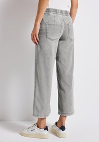 Pantalons gris à jambes larges avec une taille élastique, poches arrières et une texture douce, associés à des baskets blanches avec des accents navy.