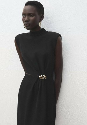 Robe noire sans manches avec un col haut, présentant une découpe sur le côté et un accent en métal doré à la taille. Texture de tissu lisse.