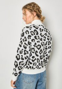 Biały sweter w czarne printy w panterkę, teksturowana dzianina, prążkowane mankiety i dół, o luźnym kroju i okrągłym dekolcie.