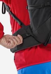 Schwarzer Rucksack mit verstellbarem Hüftgurt, der aus strukturiertem Material besteht und eine rote Basisschicht mit einem Wabenmuster hat.