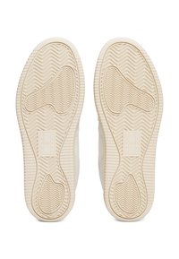 Krémové podrážky tenisek s texturovanými úchopy, s cik-cak vzory a obdélníkovým logem s vyraženými slovy "TOMMY" a "JEANS".