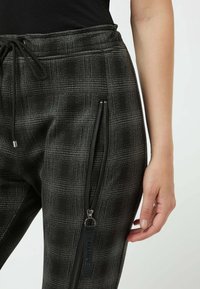 Svarta joggers med ett texturerat rutmönster, med sidofickor med dragkedja och ett justerbart midjeband med snörning. Slät tygfinish.