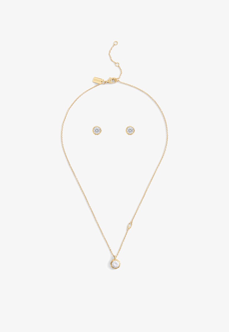 Set di gioielli in tonalità oro, composto da una delicata collana a catena con un pendente rotondo e orecchini a bottone, ciascuno decorato con una pietra trasparente.