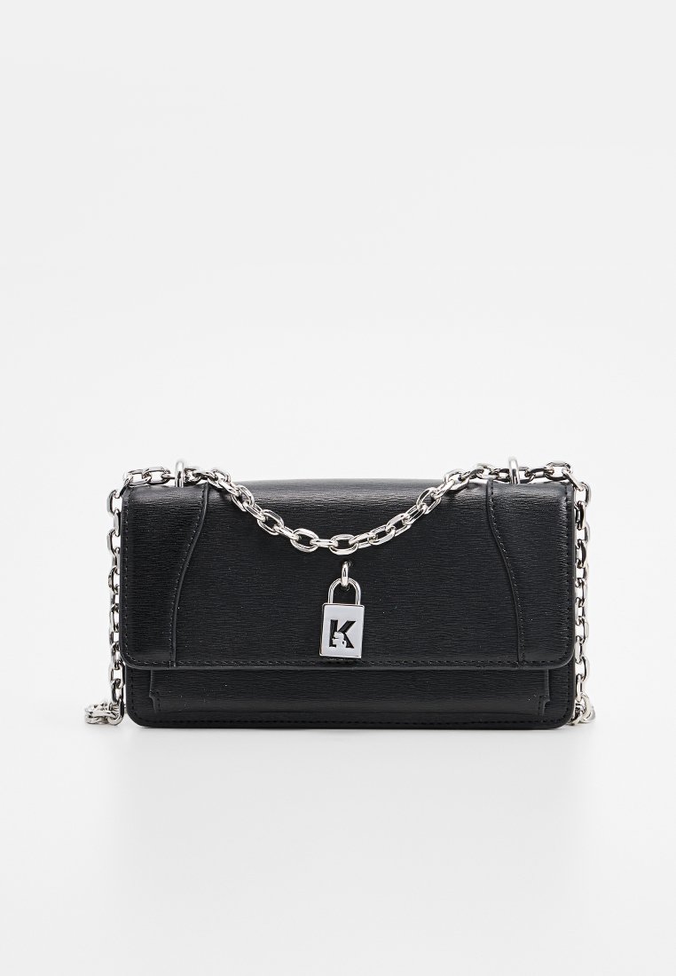 Pochette en cuir noir avec une chaîne en métal argenté et un fermoir en forme de cadenas arborant un K découpé, sur fond blanc.