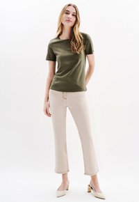 Olijfgroene top met korte mouwen en een relaxte fit, gecombineerd met lichtbeige cropped jeans. Het model draagt crème-kleurige blokhak schoenen.