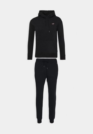Sweat à capuche noir avec poche avant et pantalon de jogging noir assorti avec taille à cordon, tous deux avec petit logo sur la poitrine et la hanche.