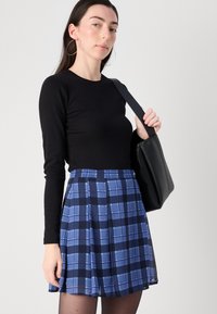 Black long-sleeve top paired with a blue plaid skirt featuring varying shades of blue and black, and a solid black shoulder bag.
