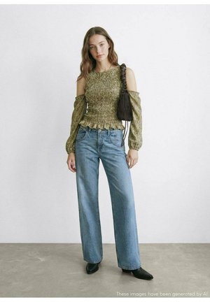 Top verde oliva con arrugas, maniche a sbuffo scoperte e orlo arricciato; abbinato a jeans azzurri a gamba larga e stivaletti neri.