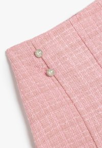 Vaaleanpunainen tweed-kangas, jossa on kaksi helmityyppistä nappia vyötäröllä, tekstuuritietoa ja hienovarainen kuvio läpi kuden.