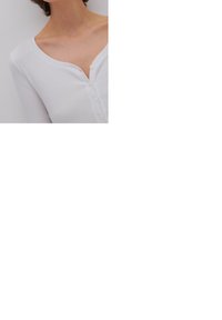 White ribbed long-sleeve top with a deep V-neckline and five buttons down the front. Soft texture and fitted design.