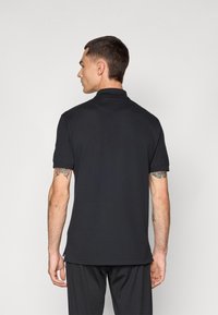 Sort polo shirt lavet af glat stof, med krave og korte ærmer. Ribbede manchetter og lige kant med subtile sideslidser.