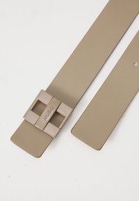 Beige öv négyzet alakú csattal, amelyen a "HUGO" felirat található. Sima anyagból készült, lapos, minimalista dizájnnal.