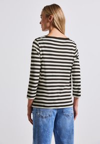 Gestreiftes langärmliges T-Shirt in Dunkelgrün und Creme, mit einem Bootsausschnitt und Dreiviertelärmeln, kombiniert mit hellblauen Jeans.