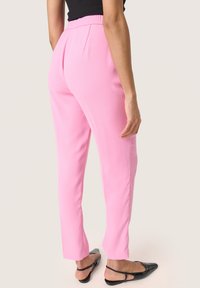 Pantaloni rosa su misura con una texture liscia, caratterizzati da una vita alta e gambe affusolate, abbinati a scarpe nere slip-on.