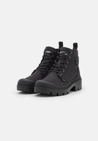 Bottes noires à la cheville avec tige en toile, semelle en caoutchouc, lacets proéminents et un patch logo sur le côté. Semelle profilée pour une meilleure traction.