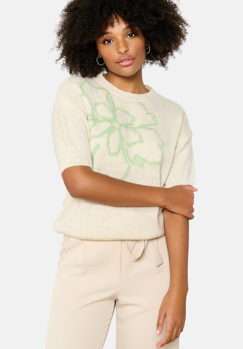 Short-sleeve cream sweater with green floral pattern, made of soft, textured material. Accented with a round neckline and relaxed fit.