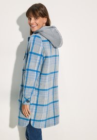 Cappotto grigio a quadri con motivo a righe blu e bianche. Presenta un cappuccio trapuntato grigio e polsini con bottoni. Texture morbida e design lungo fino al ginocchio.