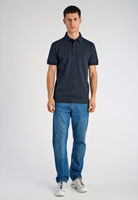 Granatowa koszulka polo o rypsowej fakturze, z krótkimi rękawami i plisą na trzy guziki, połączona z niebieskimi dżinsami i białymi trampkami.