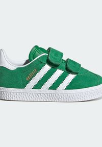 Green suede sneaker with white stripes, dual Velcro straps, white textured sole, and gold "Gazelle" branding on side.