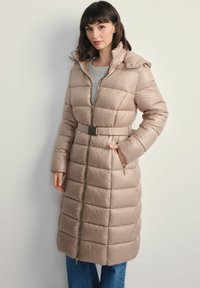 Beżowy płaszcz z podszewką, z odpinanym kapturem, z paskiem w talii, w pionowe pikowania oraz złotym zamkiem błyskawicznym. Posiada kieszenie po bokach i długie rękawy.