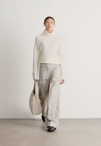 Camisola creme de gola alta, calças largas aos quadrados em cores suaves e mala tote cinzenta. O modelo usa sapatos pretos, com texturas suaves e minimalistas.