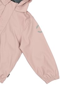 Chaqueta impermeable rosa con capucha, puños elásticos y un detalle del logo gris en la manga; textura suave y diseño moderno.