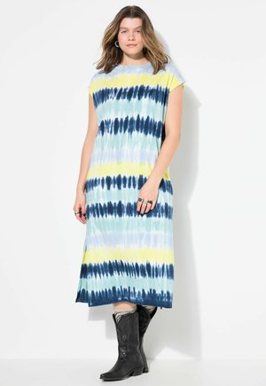 Vestido maxi de teñido anudado que presenta una mezcla de colores azul, amarillo y verde, con mangas cortas y un corte relajado. Combinado con botas de cowboy negras.