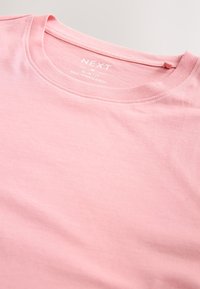 Slim fit lyserød t-shirt lavet af blødt stof, med rund halsudskæring og mærkedetalje ved kraven, glat tekstur over det hele.