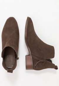 Hnědé nubukové kotníkové boty se špalíkovými podpatky, bočním zipem a poutkem, zobrazené z horního a bočního pohledu na bílém pozadí.